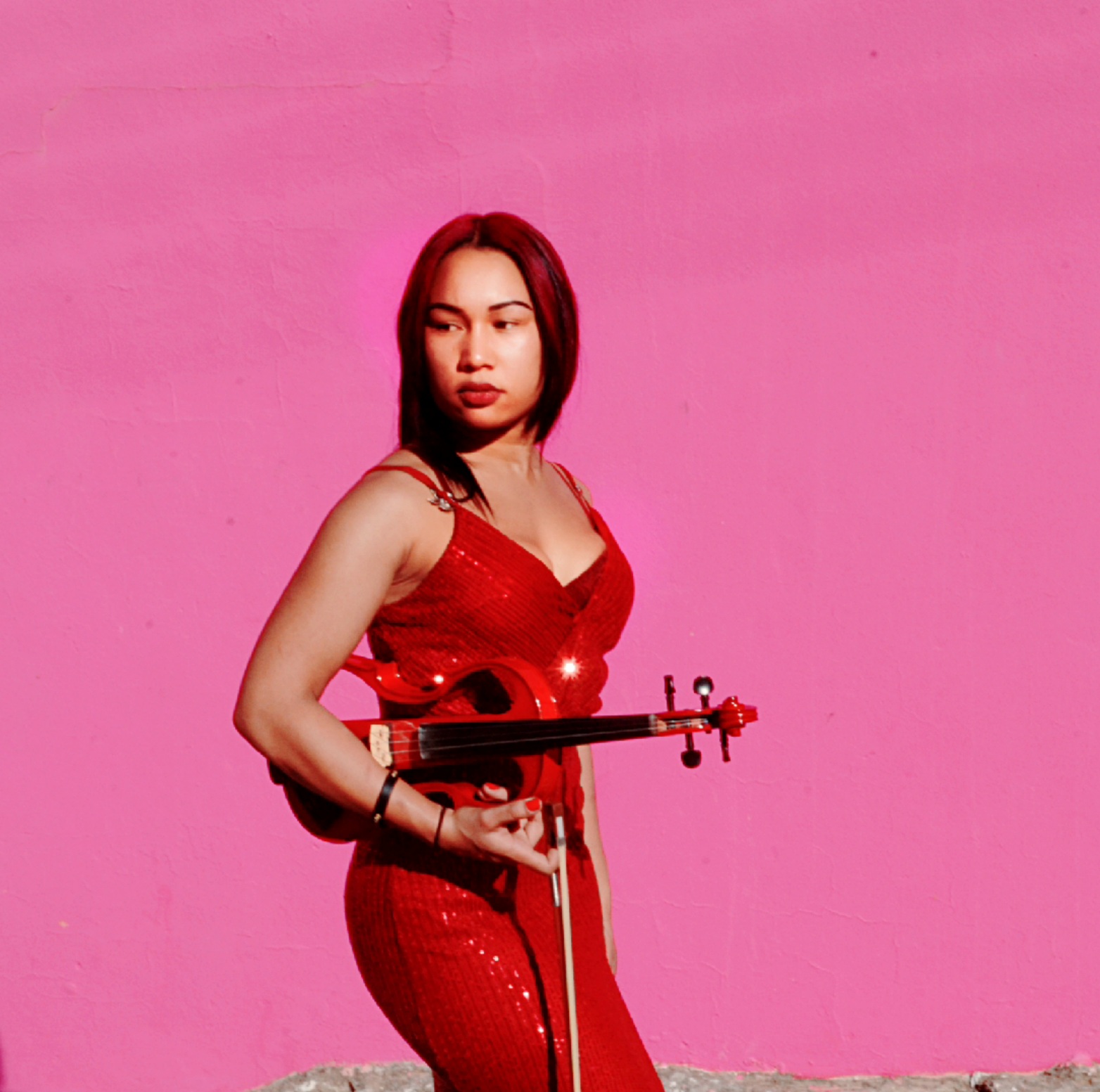 Estée Carter Adams performing on electric violin against a pink wall